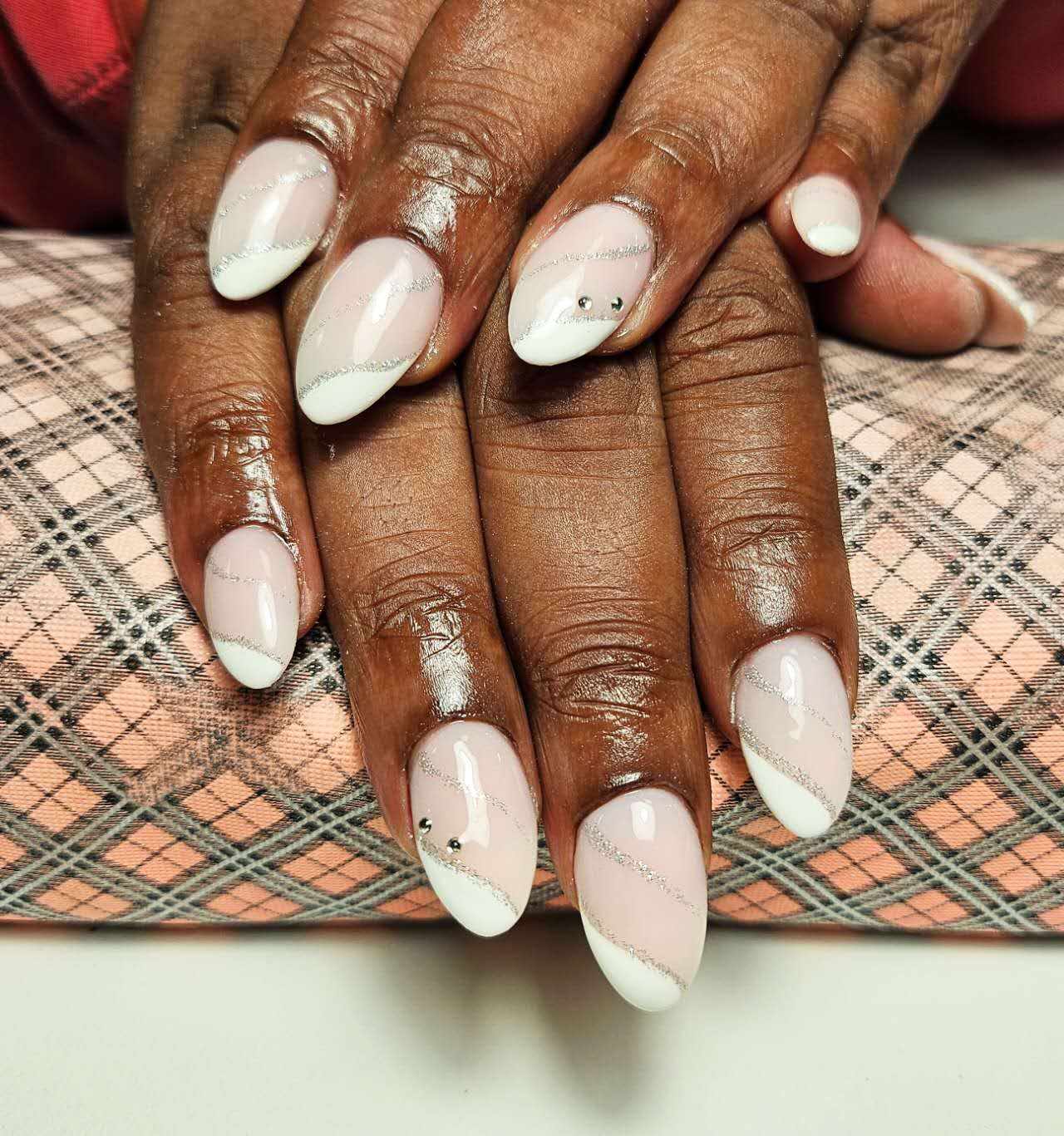 Amandelvormige nagels, wit schuin over een nude basis met kleine steentjes, op het roze armkussen