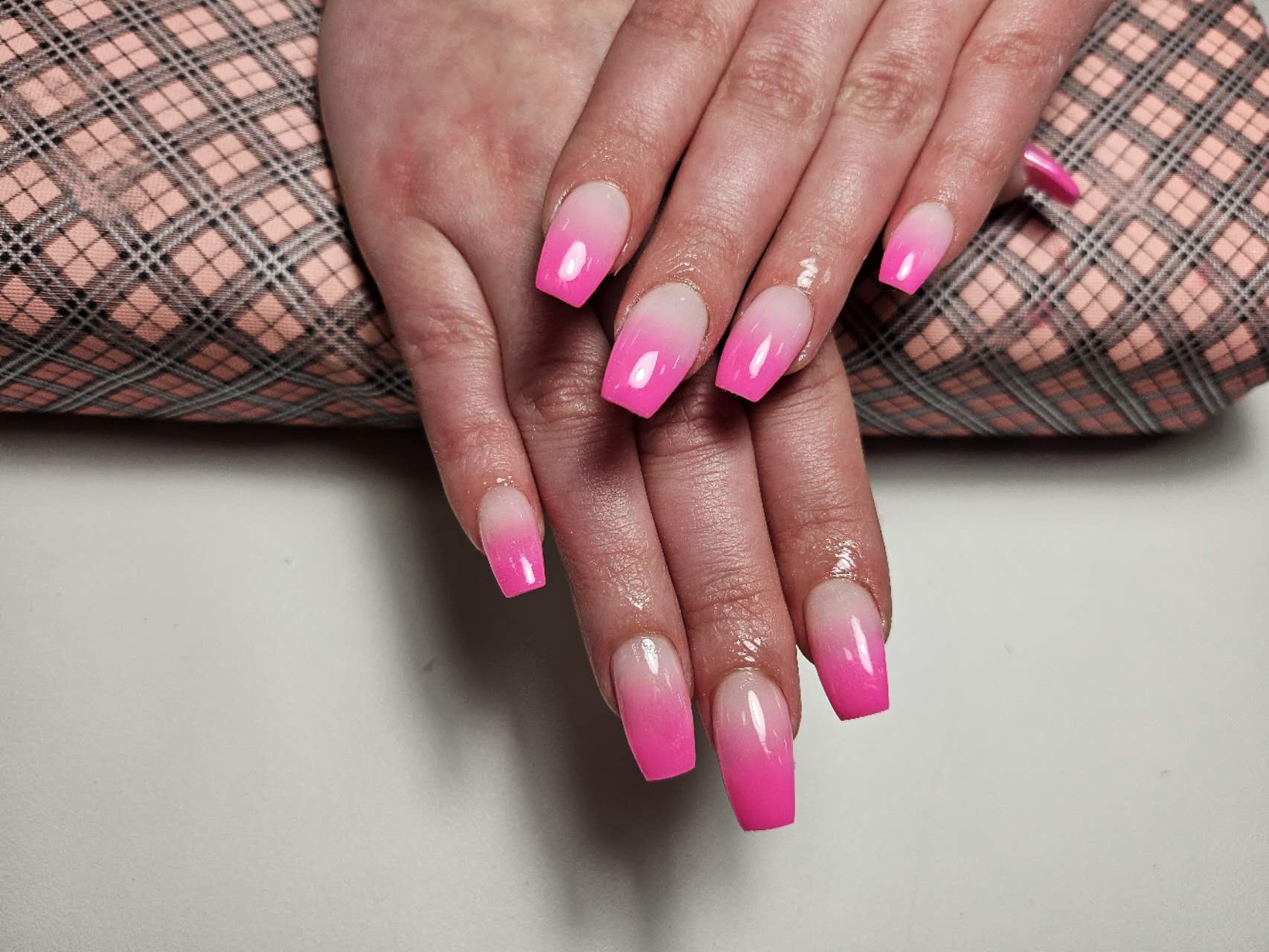 Nagels in een roze ombré, van nude naar felroze, op het roze armkussen
